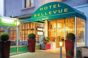 Hotelli nimeltä ”Hotel Bellevue”, jossa on vihreä markiisi, suuret ikkunat ja etupuolella ruukuissa olevia kasveja.