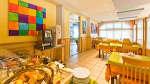 Ein Hotel-Speisesaal mit Buffet, Tischen, Stühlen und einem farbenfrohen Wandbild.