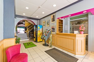 Hotellin aula, jossa on vastaanottotiski, portaikko ja vihreä matto, jossa on logon kuvio.