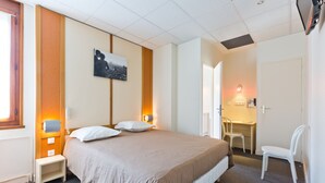 Ein Hotelzimmer mit Bett, Nachttisch, Stuhl, Schreibtisch und einem an der Wand befestigten Telefon.