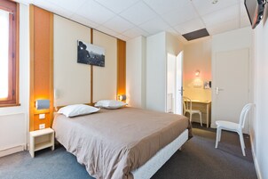 Hotellihuone, jossa on sänky, yöpöytä, tuoli, työpöytä ja seinälle asennettu puhelin.