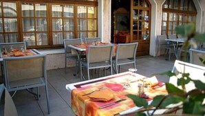 Ein Essbereich im Freien mit Tischen und Stühlen, ein Gebäudeeingang und ein Fenster mit Vorhängen.