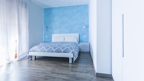 A bedroom with a bed, wooden flooring, a blue accent wall, and a white bedside table. - B&B La Postale (San Salvo)