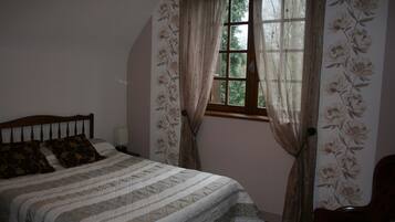 Een slaapkamer met een bed, nachtkastje, stoel en raam met gordijnen.