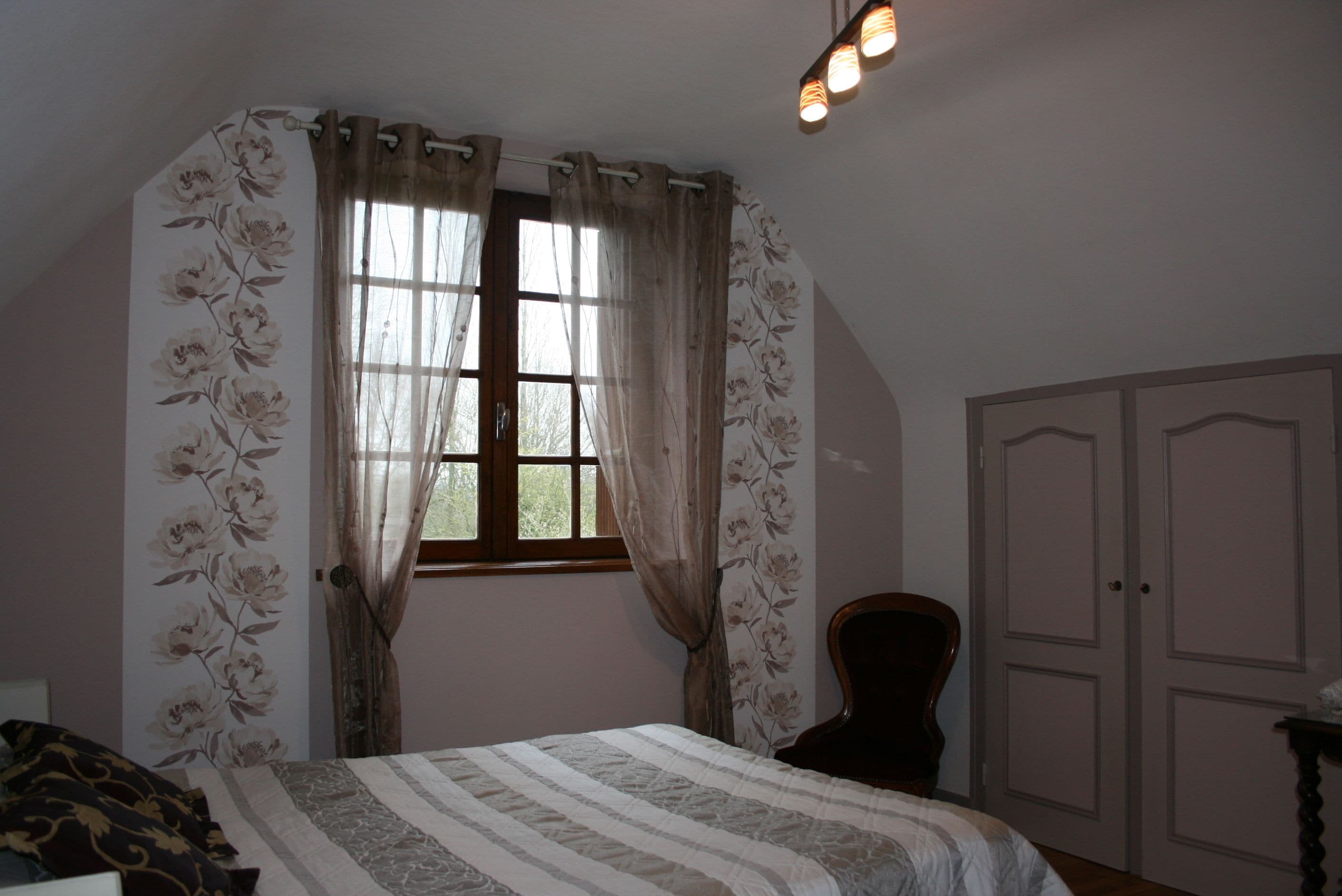 Ein Schlafzimmer mit Bett, Stuhl, Kleiderschrank und einem Fenster mit Vorhängen.