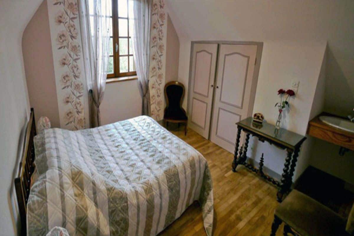 Un dormitorio con cama, una silla, cómoda y ventana con cortinas.