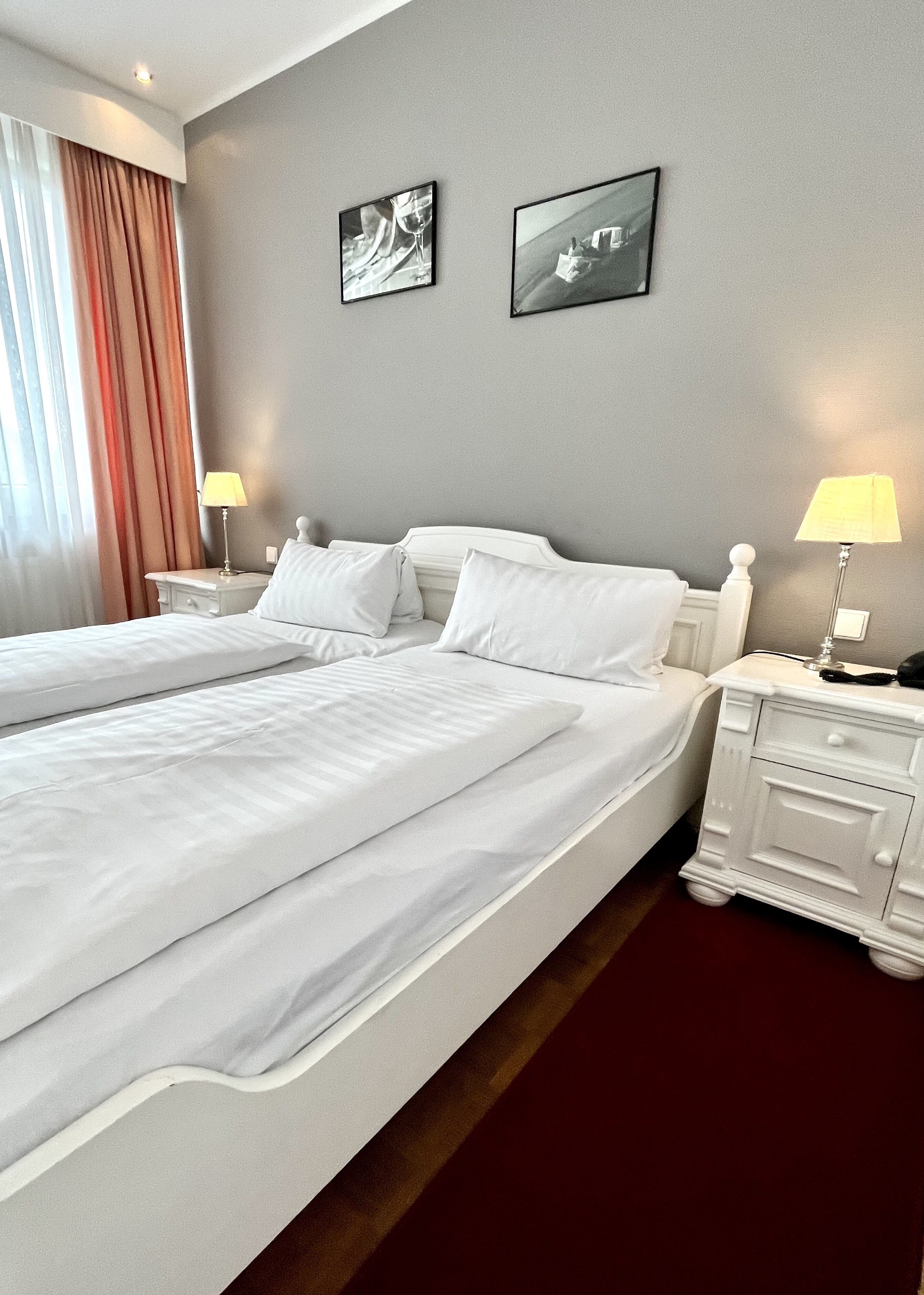 Ein Hotelzimmer mit zwei Betten, einem Nachttisch mit Lampe und zwei gerahmten Bildern an der Wand.