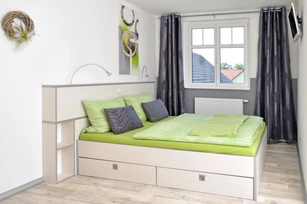 A bedroom with a bed, a radiator, a window, and curtains.