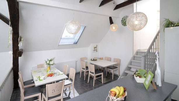 Un comedor con una mesa dispuesta para dos, una cesta de frutas sobre la mesa y una escalera al fondo.