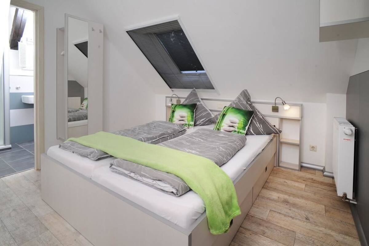 A bedroom with a bed, a skylight, a bedside table, and a radiator.