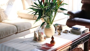 A cozy living room with a sofa, a coffee table with decorative items, and a view through large windows. - Villa Darakorn (Chiang Rai)