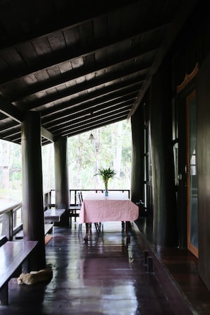 A covered outdoor area with a checkered table, wooden pillars, and a view of greenery. - Villa Darakorn (Chiang Rai)