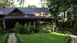 A traditional wooden house with a sloped roof, surrounded by a well-maintained garden with a gravel path leading to the entrance. - Villa Darakorn (Chiang Rai)