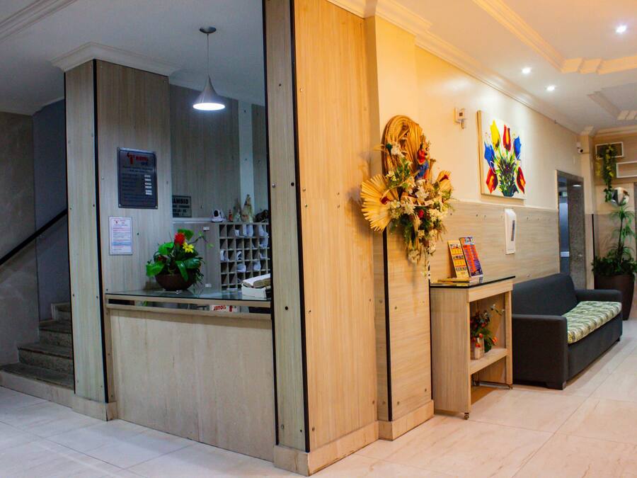 Un área de recepción con mostrador de madera, escalera, sofá y una pared decorada con un arreglo floral y un cuadro.