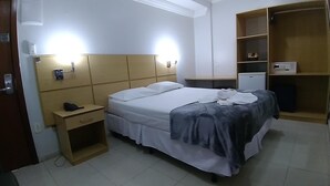 Ein Hotelzimmer mit Bett, Nachttisch, Kleiderschrank und einem kleinen Schreibtisch mit Lampe.
