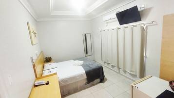 Habitación de hotel con cama, escritorio con teléfono, televisor montado en la pared y cortina de ducha.