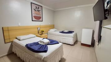 A hotel room with two beds, a small bedside table with a phone and a vase of flowers, a television, and a refrigerator.
