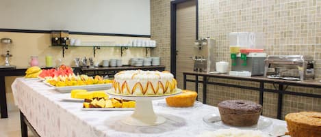 A buffet table with various food items including cakes, fruit, and rice.