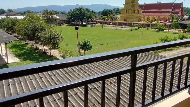 Vista desde un balcón con barandilla de metal, con vistas a un complejo de templos que incluye una gran estupa dorada y un edificio de techo rojo.