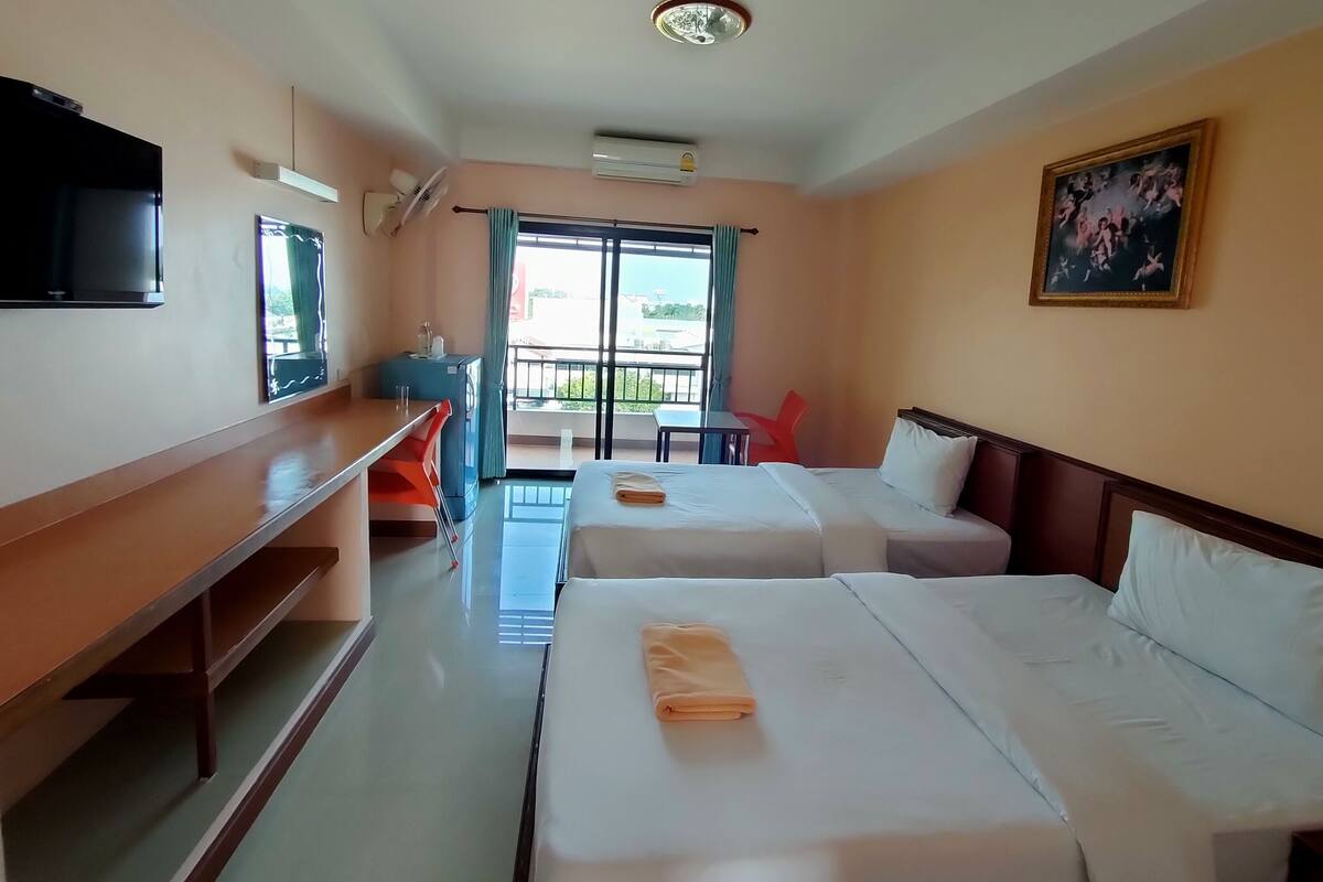 Habitación de hotel con dos camas, un escritorio, un televisor y un balcón con vistas.