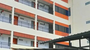 Un edificio de varios pisos con balcones, un acceso cubierto y un estacionamiento.