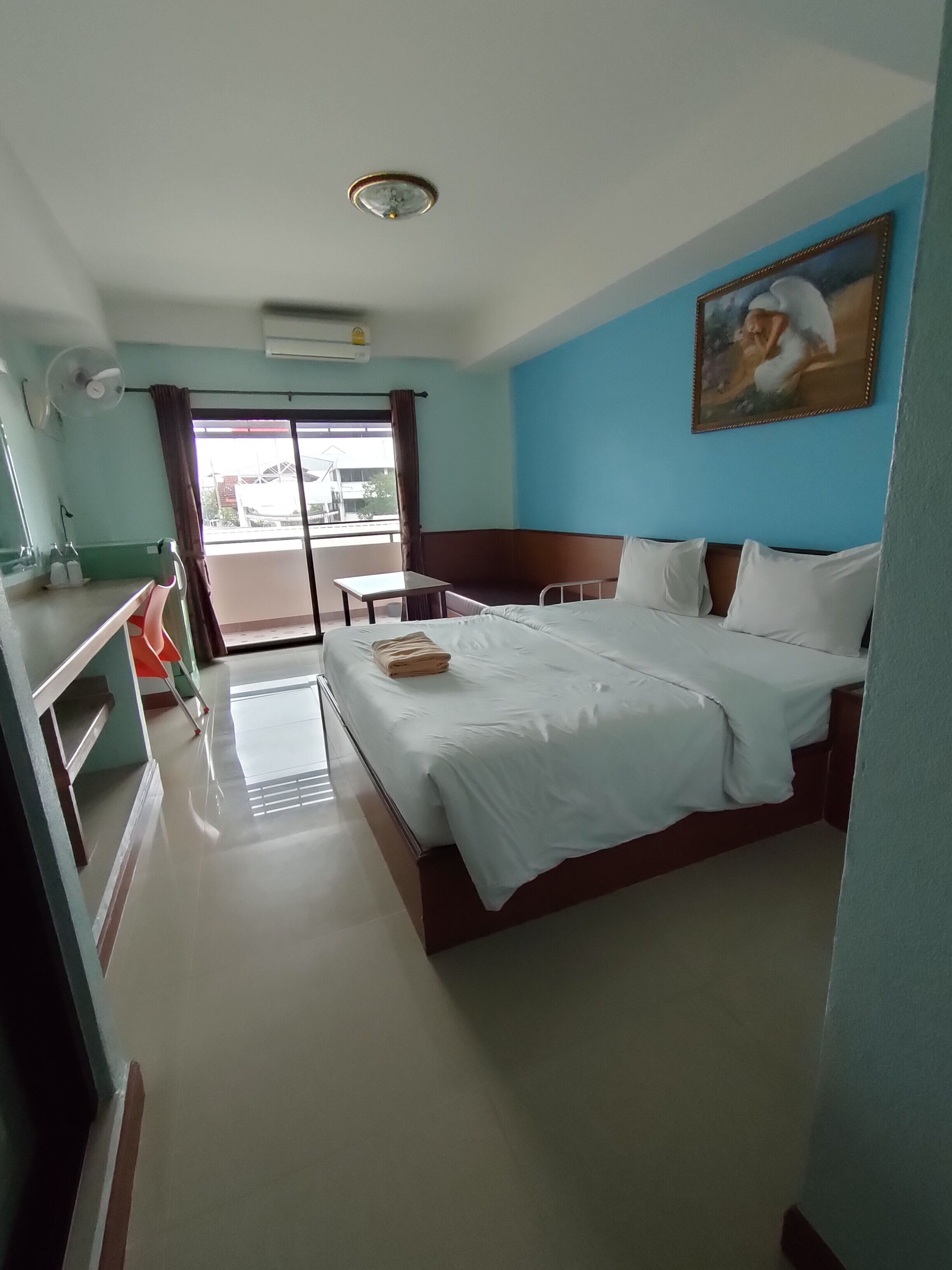 Una habitación de hotel con cama, una mesita, una silla, una ventana con cortinas y un cuadro en la pared.