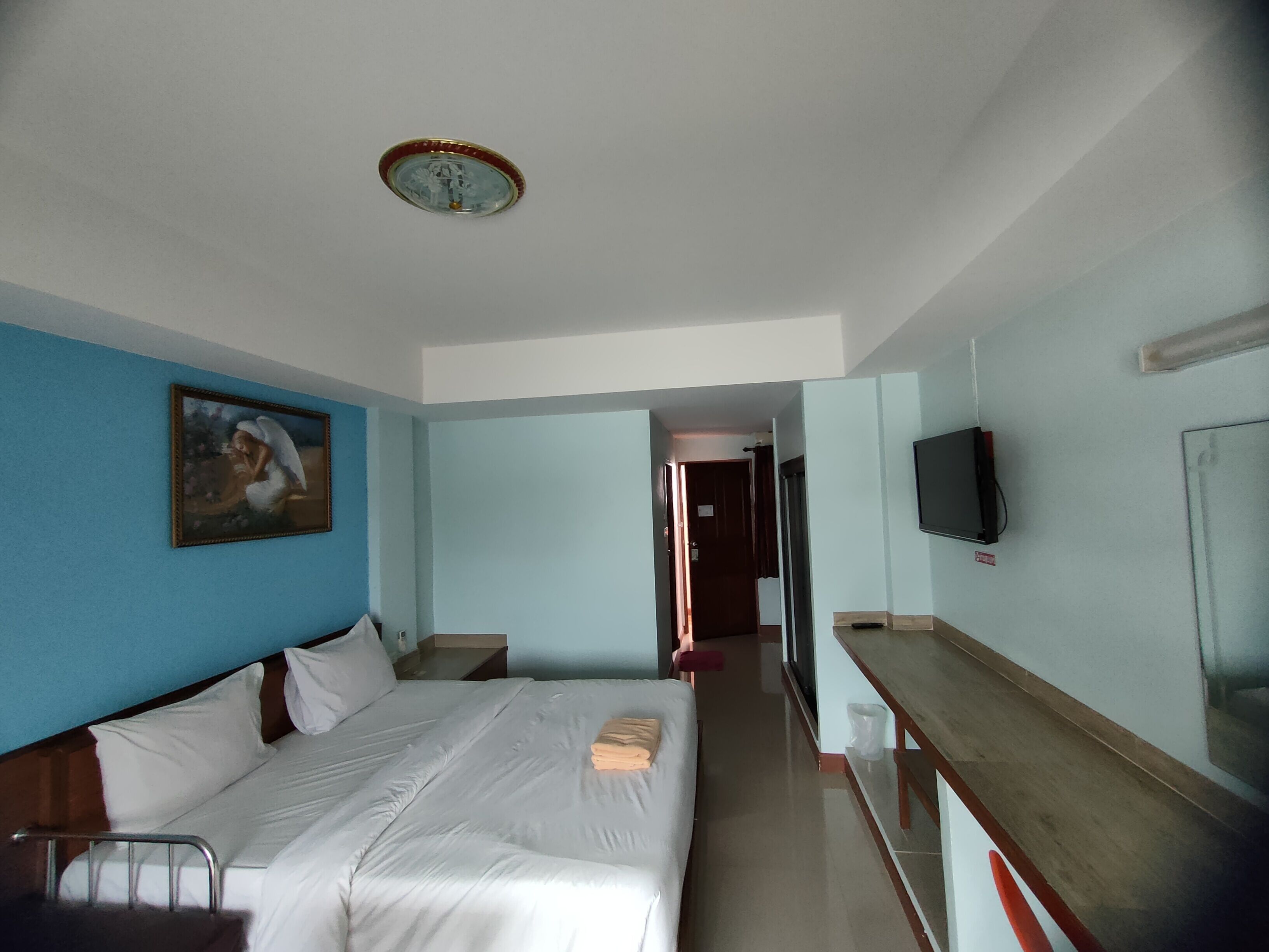 Une chambre d’hôtel avec un lit, un tableau accroché au mur, un téléviseur fixé au mur et une porte donnant sur une autre pièce.