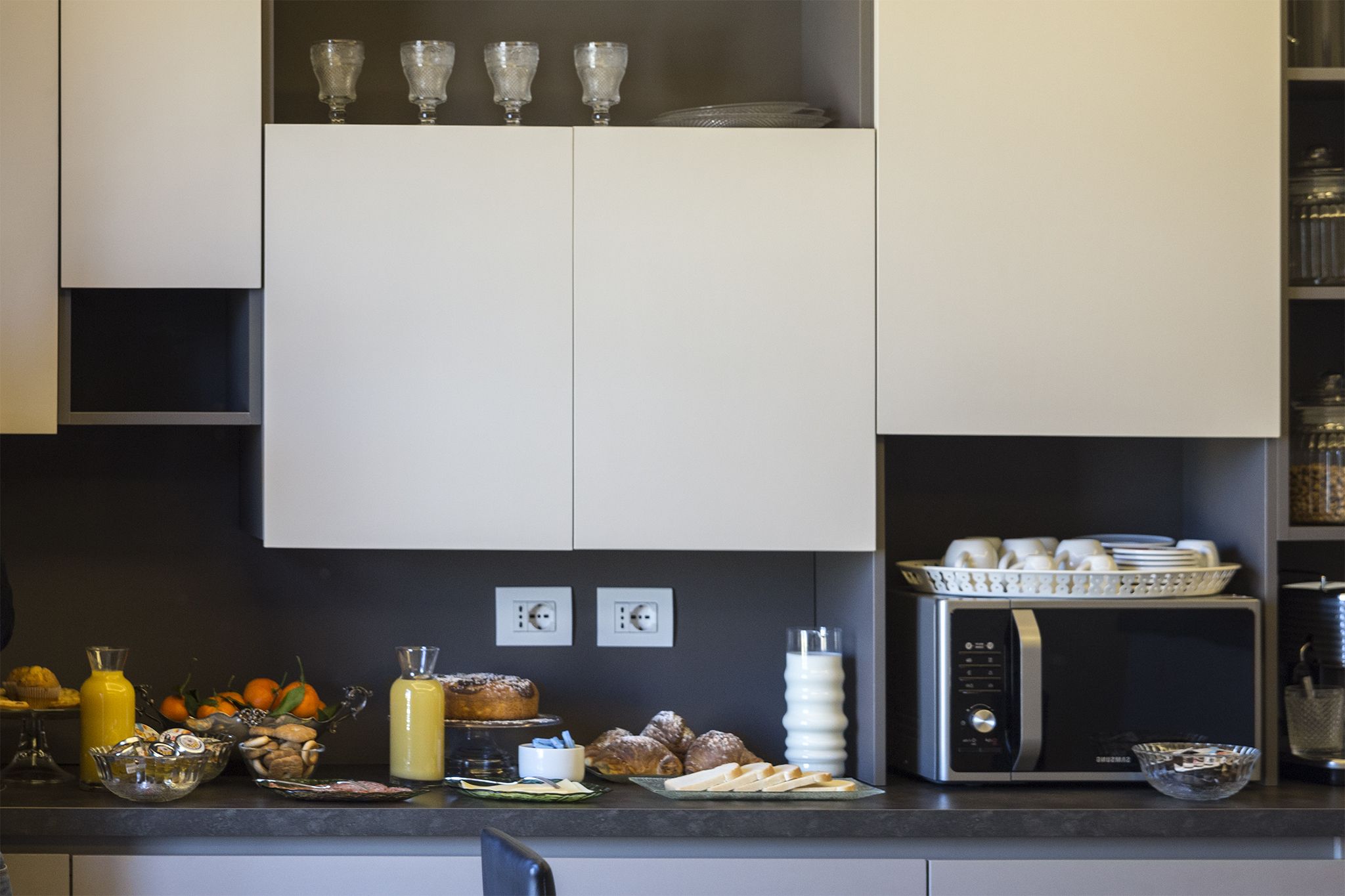 A modern kitchen with white cabinets, a microwave, and various food items on the counter.