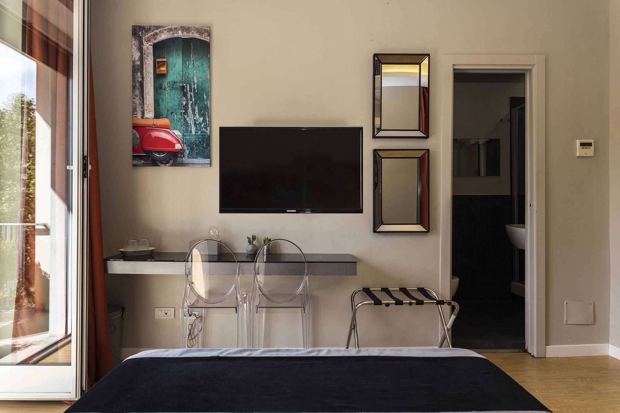 Habitación de hotel con cama, escritorio con televisor de pantalla plana, dos sillas y baño visible a través de una puerta abierta.