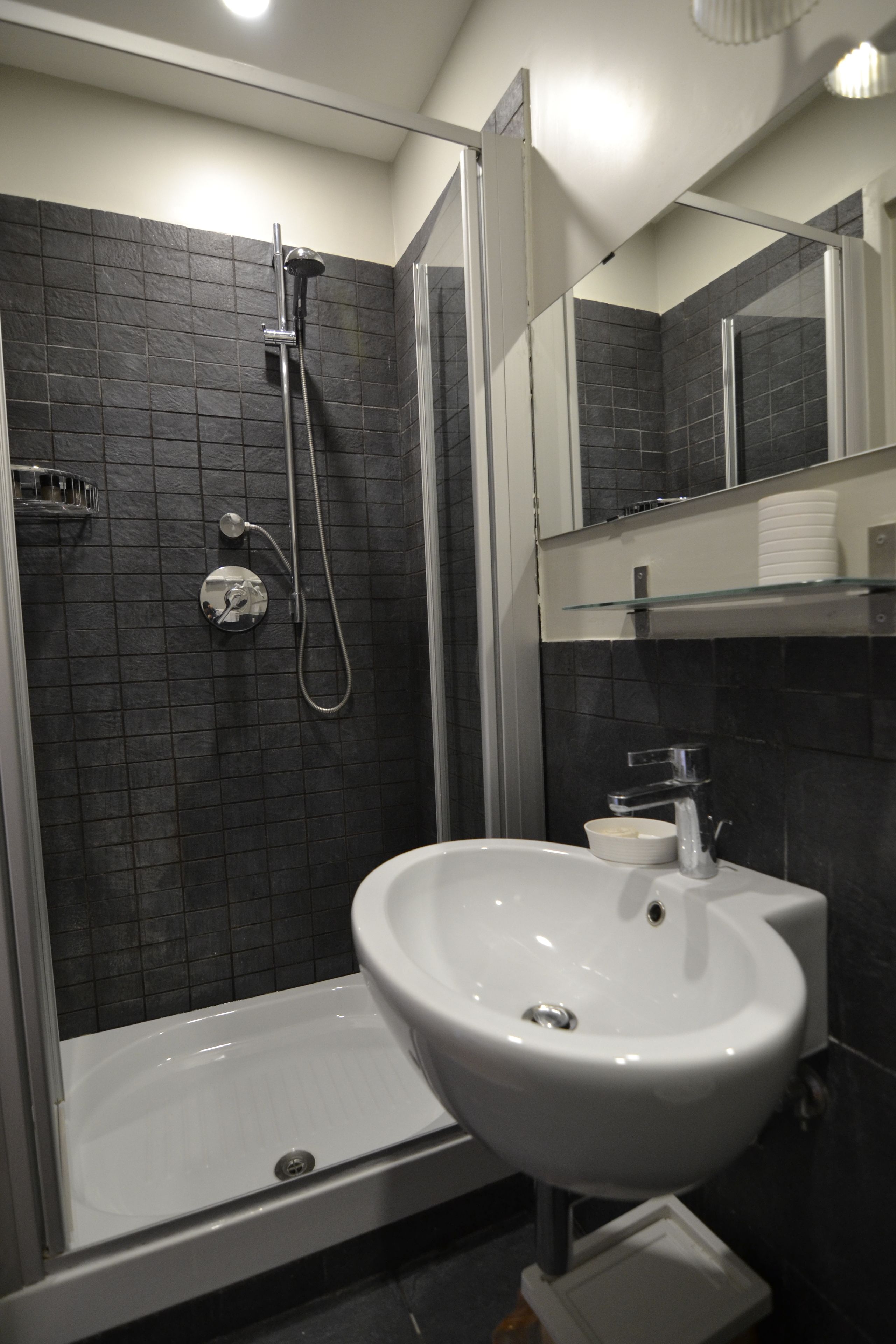 Een moderne badkamer met een douchecabine van glas, een witte wastafel en een spiegel erboven.