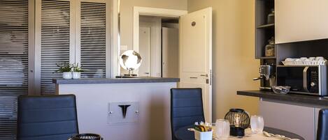 A modern kitchen with a microwave, coffee maker, and a small plant. There is a dining area with a table, chairs, and a globe decoration.