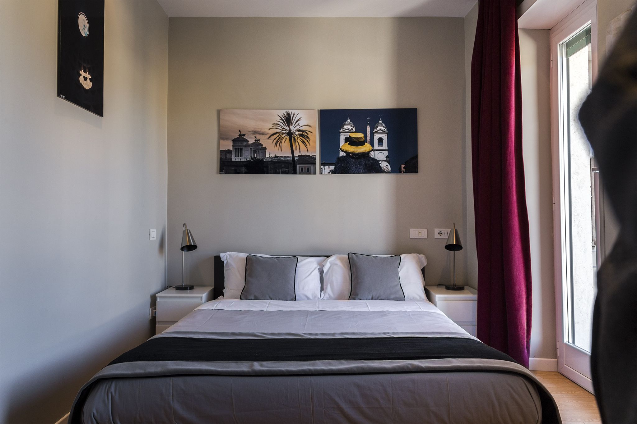 A bedroom with a bed, two nightstands, a lamp, a window with a curtain, and two wall art pieces.