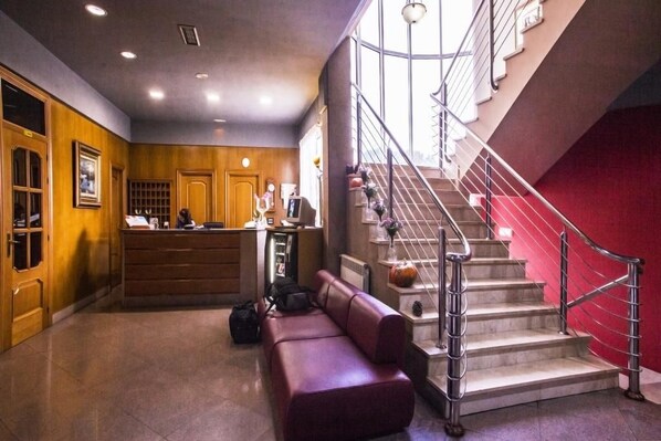 A hotel lobby with a reception desk, a red couch, a staircase with metal railings, and a wooden wall. - Hotel Las Moreras (Sariegos)