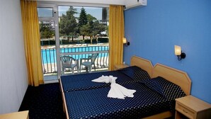 Ein Hotelzimmer mit Bett, Nachttisch, Stuhl und Blick auf Pool und Bäume.