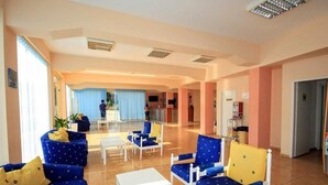 Eine geräumige Lobby mit blau-gelb gemusterten Sitzgelegenheiten, einem Empfangsbereich und Blick ins Freie.