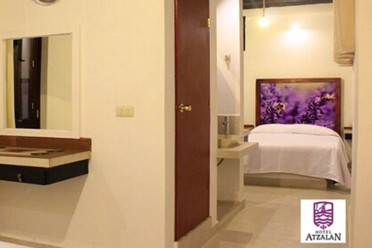 A hotel room with a bed, a bedside table, a mirror, and a bathroom with a sink.
