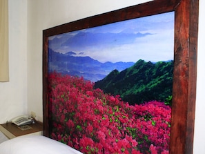 A room with a large painting of a mountainous landscape with pink flowers.