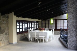A dining area with a stone wall, a wooden ceiling, and a table set with white chairs and a floral centerpiece.