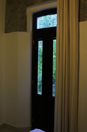 A room with a dark door, a window with curtains, and a view of greenery outside.