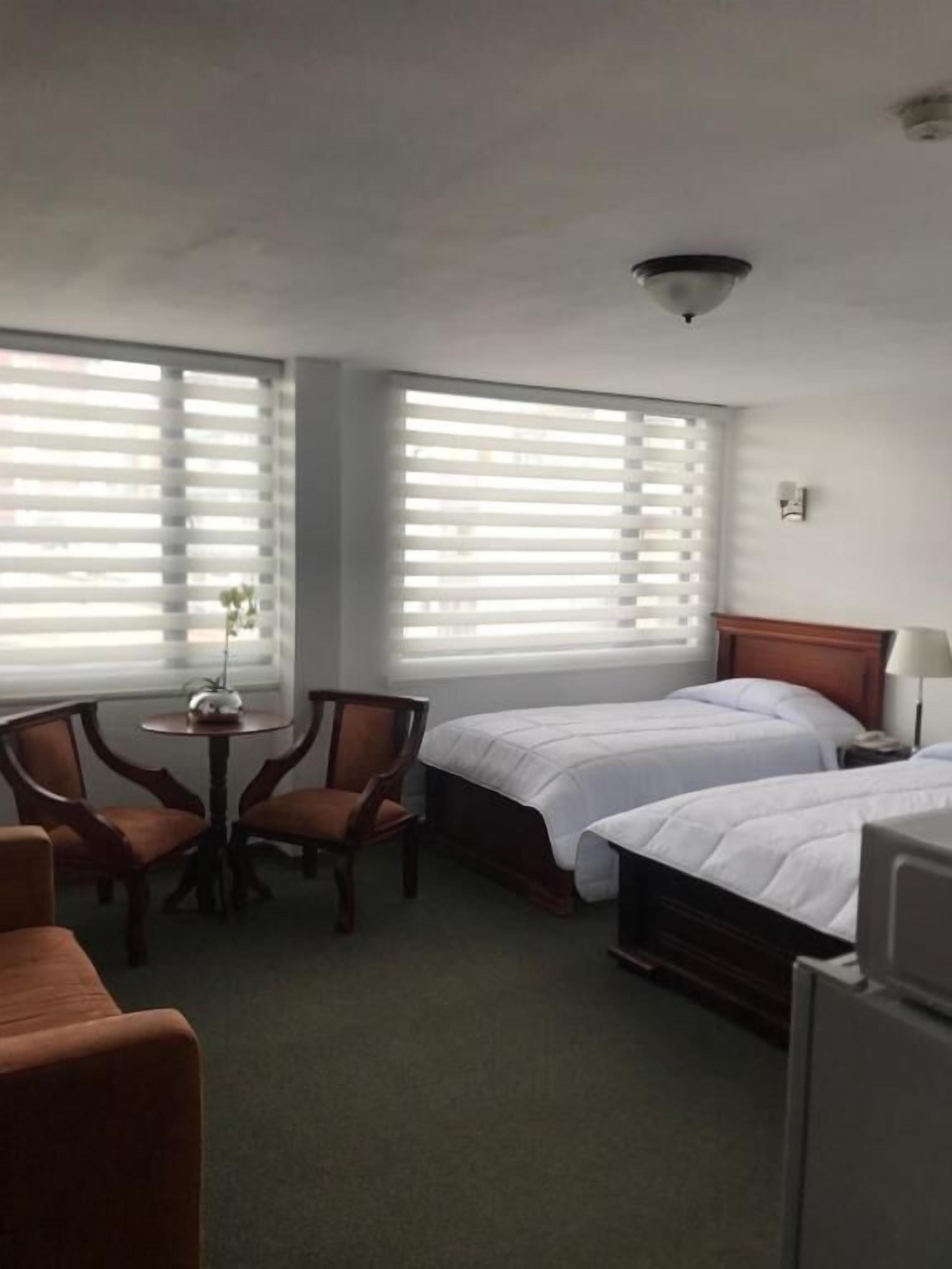Une chambre d’hôtel avec deux lits simples, une petite table avec des chaises et une grande fenêtre avec des stores.