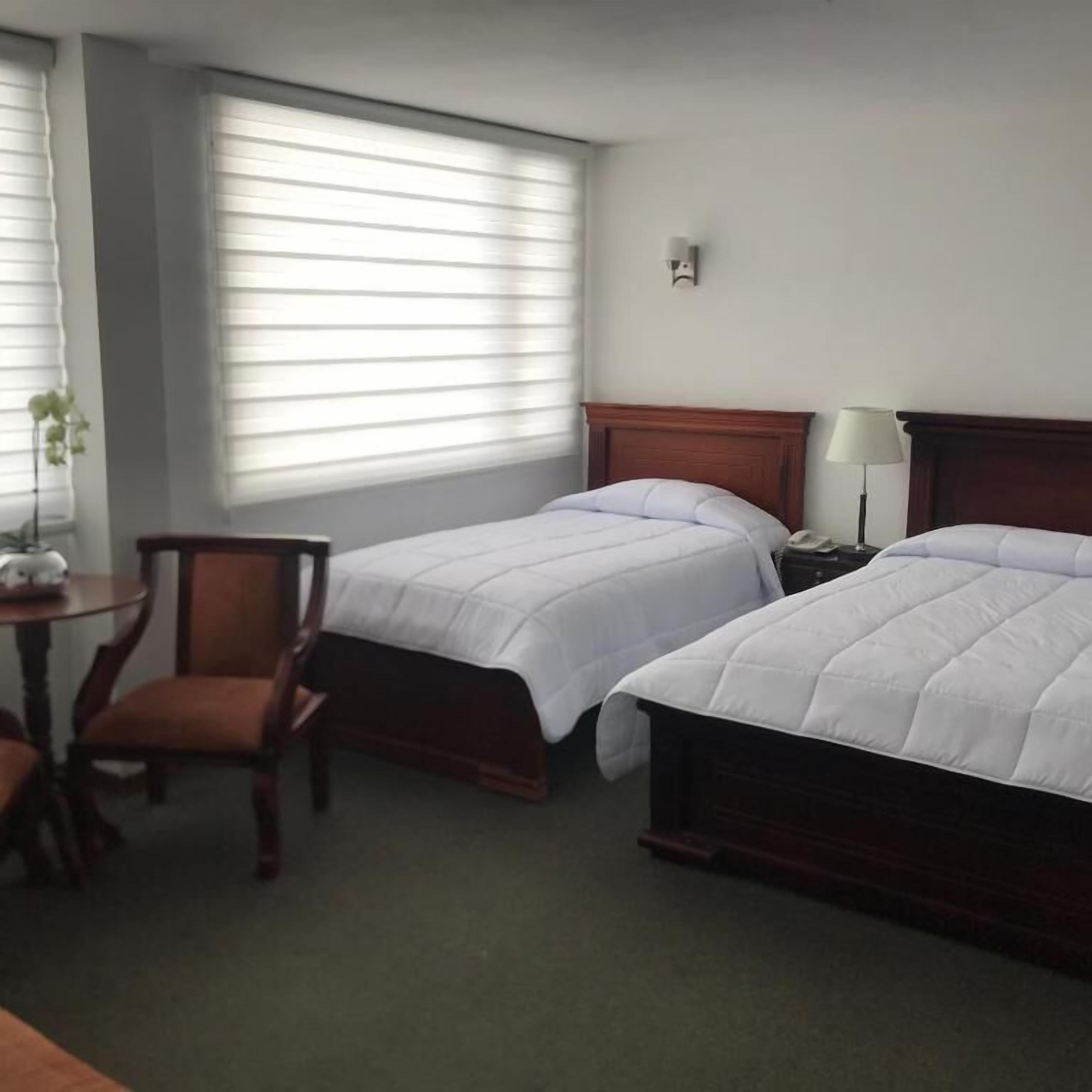 Ein Hotelzimmer mit zwei Einzelbetten, einem Holzkopfstück, einem kleinen Tisch mit Lampe und einem Sessel.