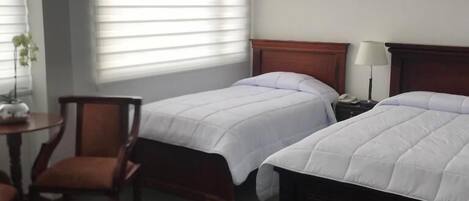 Ein Hotelzimmer mit zwei Einzelbetten, einem Holzkopfstück, einem kleinen Tisch mit Lampe und einem Sessel.