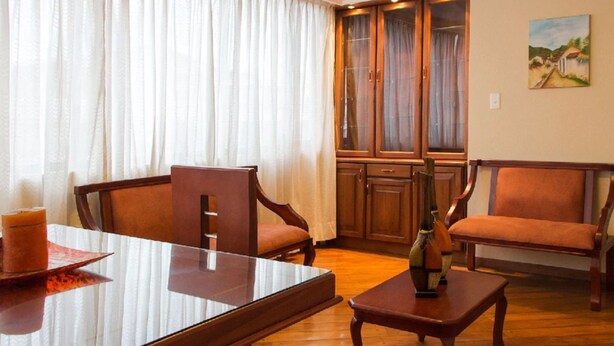 Een kamer met een houten eettafel, twee houten stoelen, een klein houten bijzettafeltje en een kast met glazen deuren.