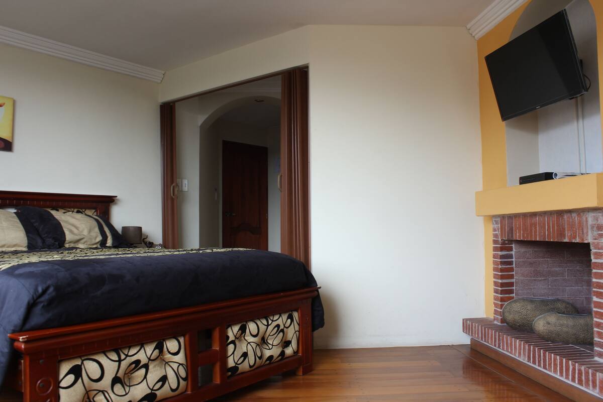 A bedroom with a bed, a fireplace, and a television mounted on the wall.