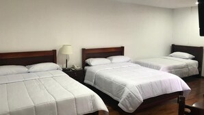 Een hotelkamer met drie enkele bedden, houten hoofdeinden en een nachtkastje met een lamp.