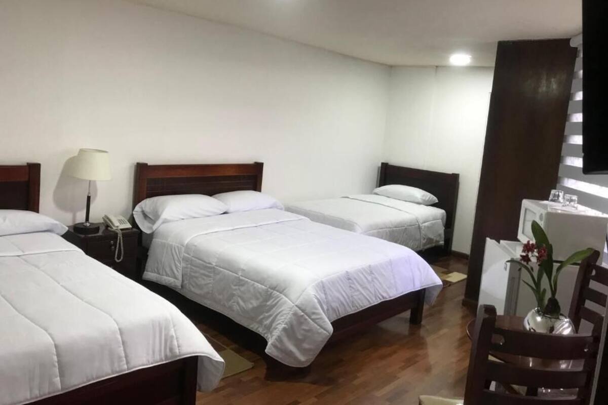A hotel room with two single beds, a wooden floor, a desk with a chair, and a small table with a vase.