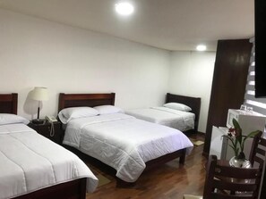 A hotel room with two single beds, a wooden floor, a desk with a chair, and a small table with a vase. - Hotel Altura (Quito)