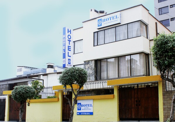 A hotel with a prominent entrance sign, a balcony with a railing, and a large tree in front. - Hotel Altura (Quito)