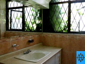 A bathroom with a sink, mirror, and window with a metal grid. - Hotel Altura (Quito)
