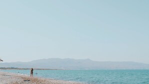 Une plage avec une personne debout sur le rivage, une mer calme et des montagnes au loin.